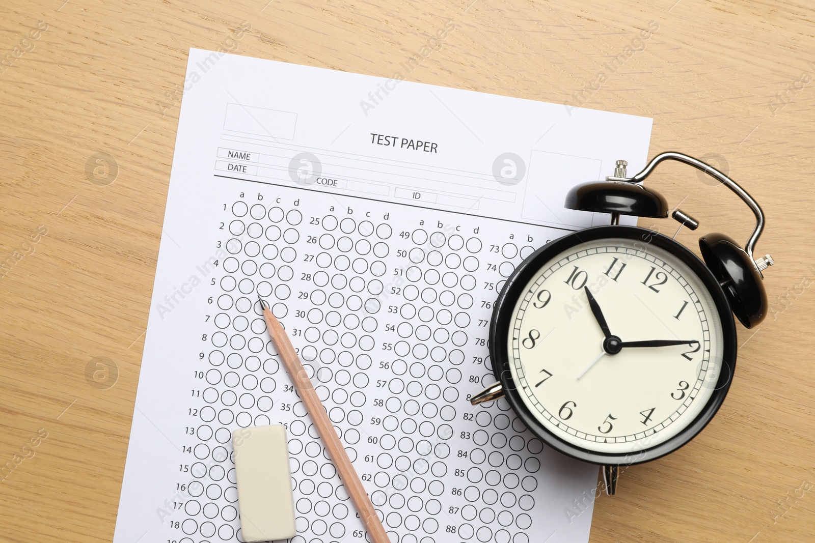 Photo of Answer sheet, eraser, pencil and alarm clock on wooden table, flat lay. Student passing exam