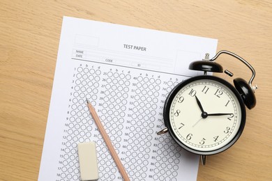 Photo of Answer sheet, eraser, pencil and alarm clock on wooden table, flat lay. Student passing exam