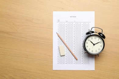 Photo of Student passing exam. Answer sheet, eraser, pencil and alarm clock on wooden table, flat lay. Space for text