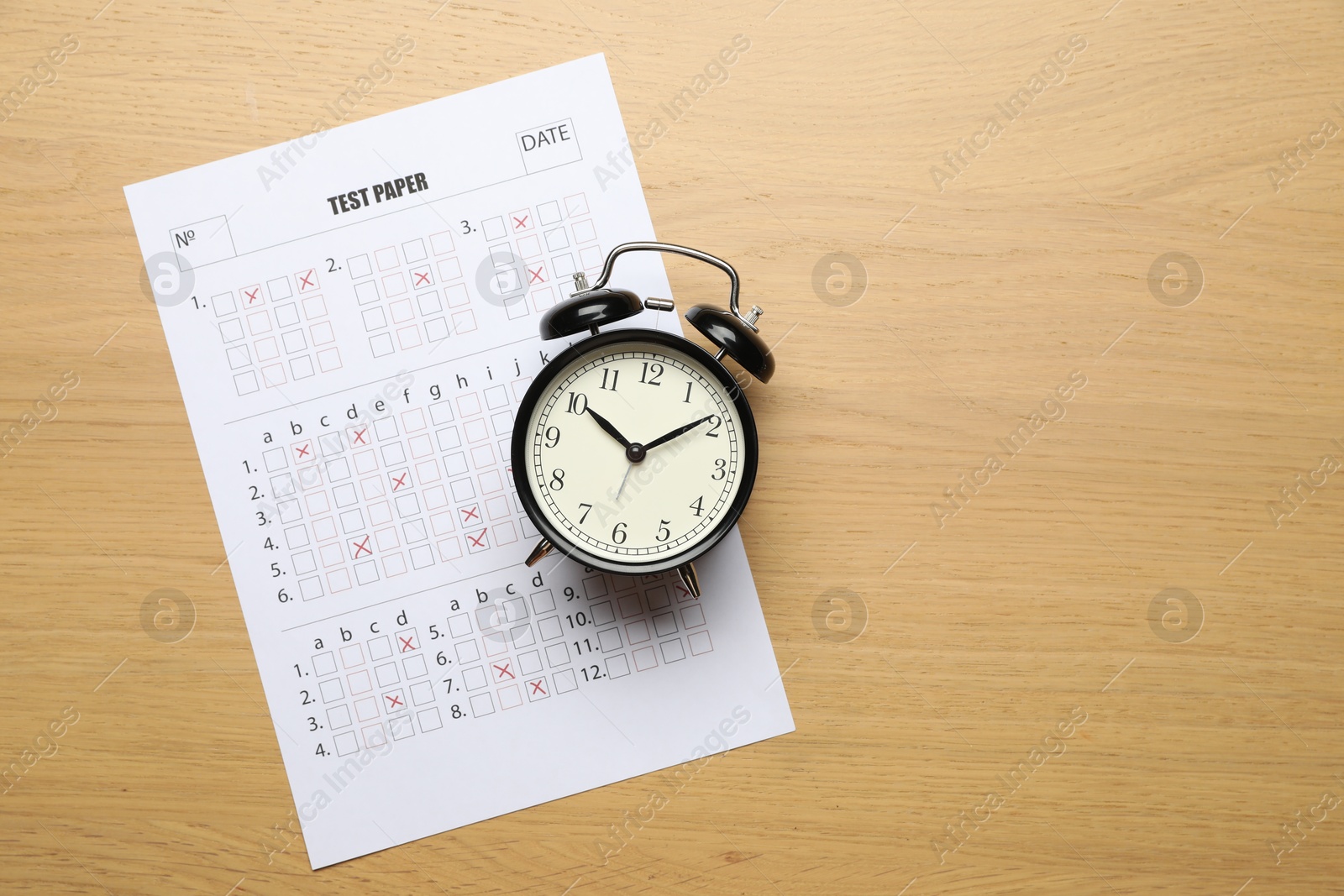 Photo of Student passing exam. Answer sheet and alarm clock on wooden table, flat lay. Space for text