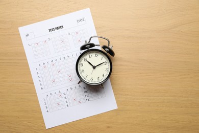 Photo of Student passing exam. Answer sheet and alarm clock on wooden table, flat lay. Space for text