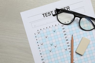 Photo of Answer sheet, eraser, pencil and glasses on wooden table, flat lay. Student passing exam