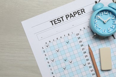 Photo of Answer sheet, eraser, pencil and alarm clock on wooden table, flat lay. Student passing exam