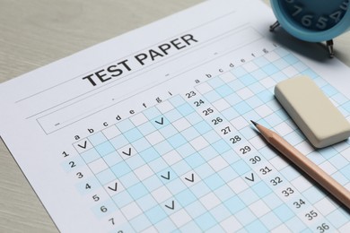 Photo of Answer sheet, eraser, pencil and alarm clock on wooden table, closeup. Student passing exam