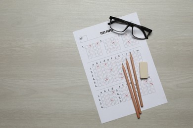 Photo of Student passing exam. Answer sheet, pencils, eraser and glasses on wooden table, flat lay. Space for text