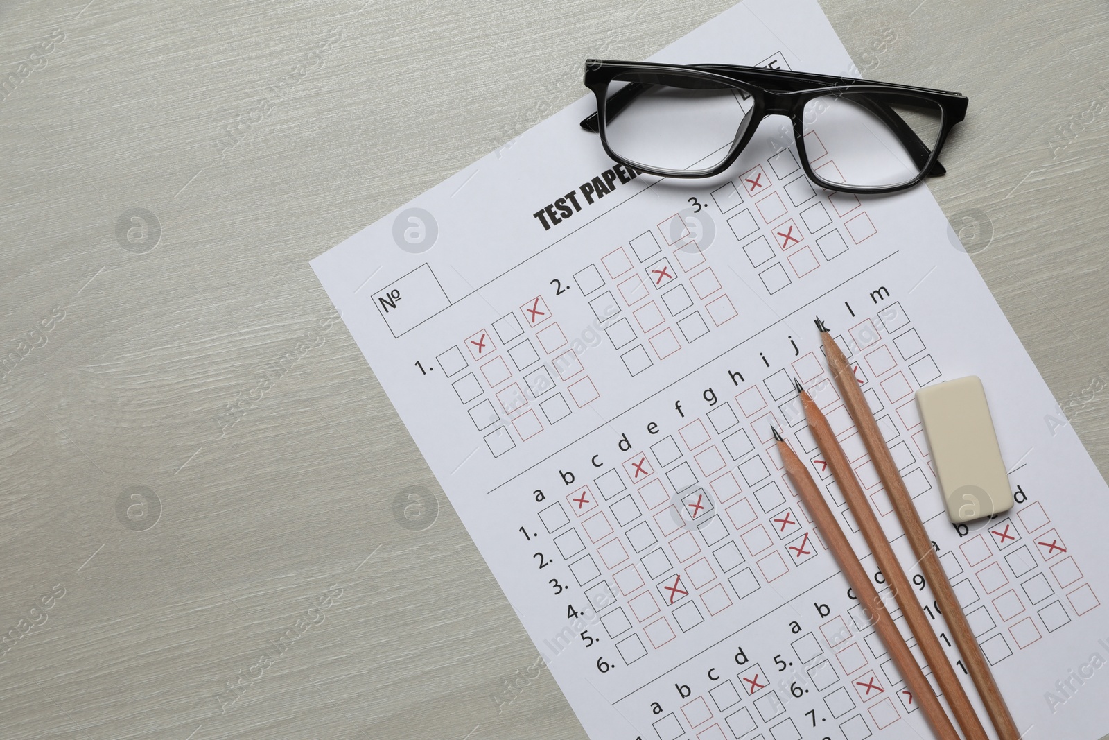 Student passing exam. Answer sheet, pencils, eraser and glasses on wooden table, flat lay. Space for text Photo of Student passing exam. Answer sheet, pencils, eraser and glasses on wooden table, flat lay. Space for text