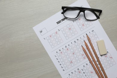 Photo of Student passing exam. Answer sheet, pencils, eraser and glasses on wooden table, flat lay. Space for text
