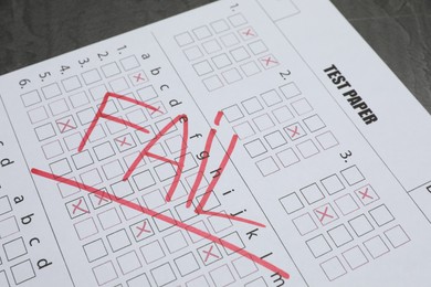 Photo of Answer sheet with word Fail on gray table, closeup. Student passing exam