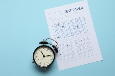 Photo of Answer sheet and alarm clock on light blue background, flat lay. Student passing exam