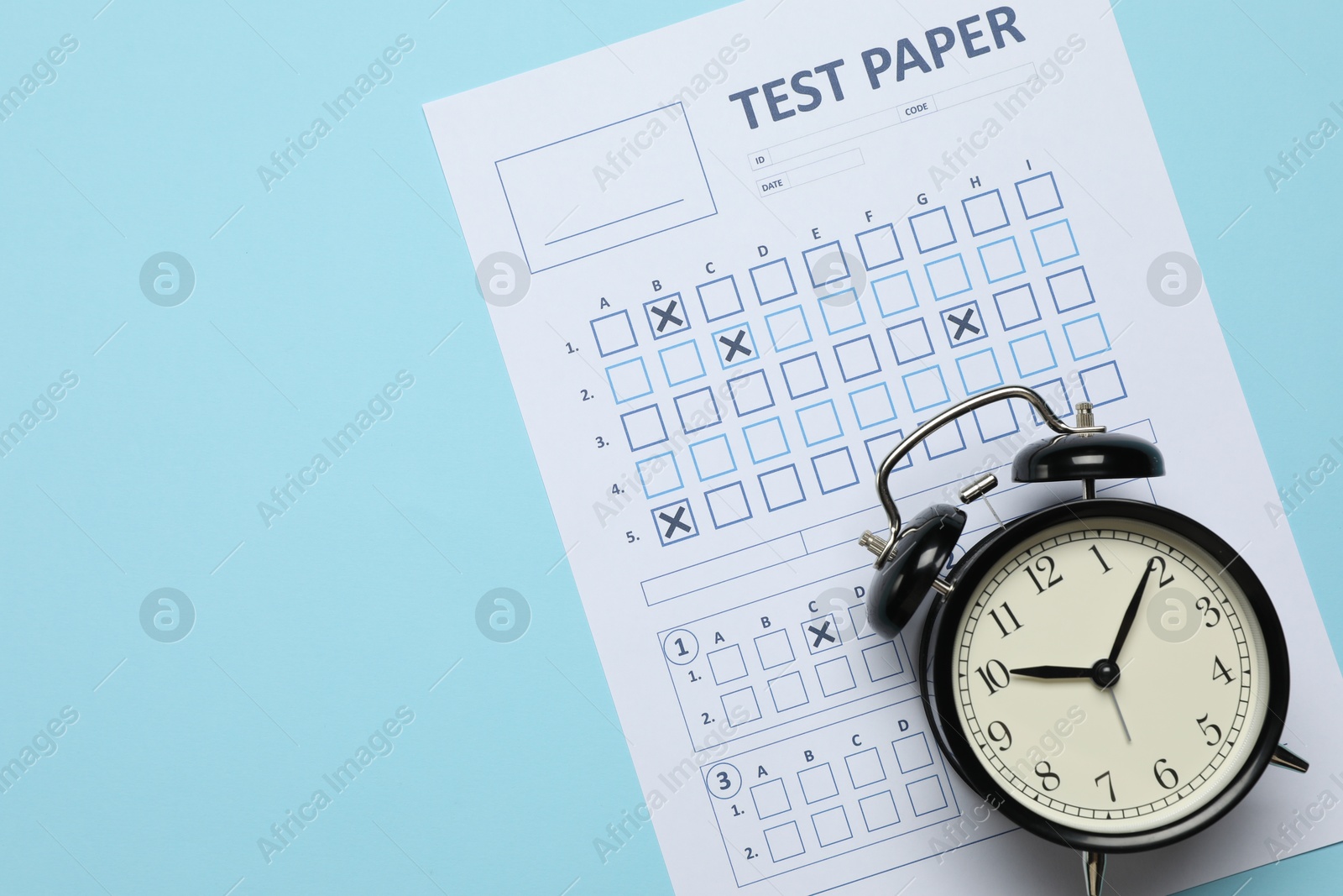 Student passing exam. Answer sheet and alarm clock on light blue background, flat lay. Space for text Photo of Student passing exam. Answer sheet and alarm clock on light blue background, flat lay. Space for text
