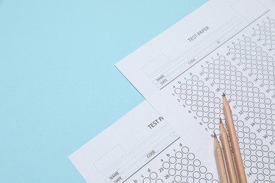 Photo of Answer sheets and pencils on light blue background, closeup. Student passing exam