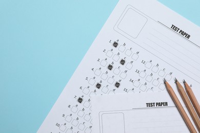 Photo of Answer sheets and pencils on light blue background, flat lay. Student passing exam