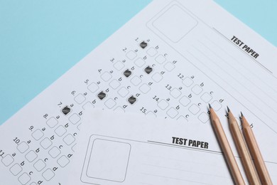 Photo of Answer sheets and pencils on light blue background, flat lay. Student passing exam