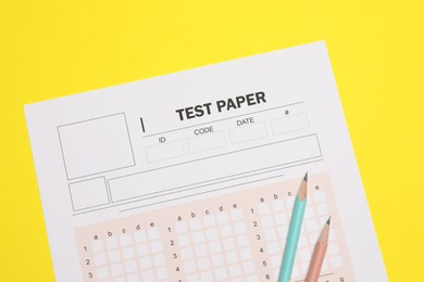 Photo of Answer sheet and pencils on yellow background, flat lay. Student passing exam