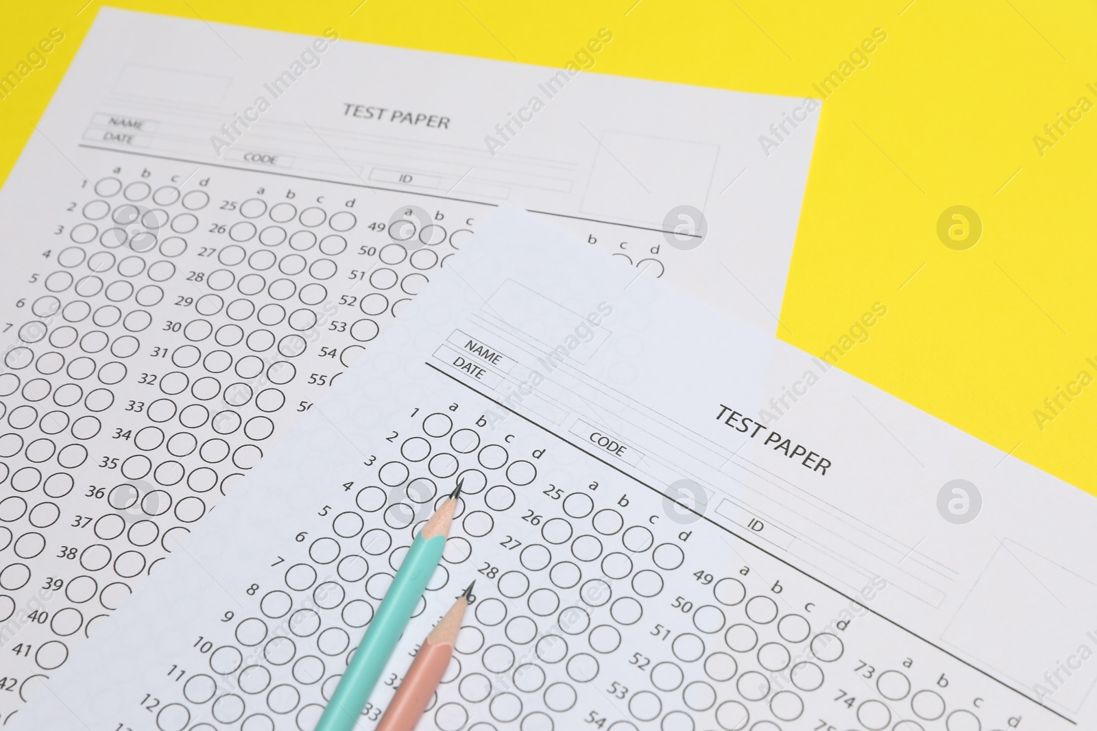 Photo of Answer sheets and pencils on yellow background, closeup. Student passing exam