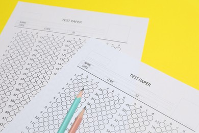 Photo of Answer sheets and pencils on yellow background, closeup. Student passing exam