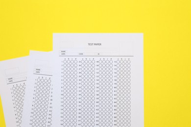 Photo of Answer sheets on yellow background, flat lay. Student passing exam