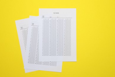 Photo of Answer sheets on yellow background, flat lay. Student passing exam