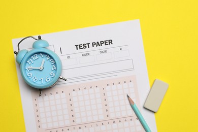 Photo of Answer sheet, alarm clock, pencil and eraser on yellow background, flat lay. Student passing exam