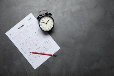 Photo of Student passing exam. Answer sheet, alarm clock and pencil on gray textured table, flat lay. Space for text