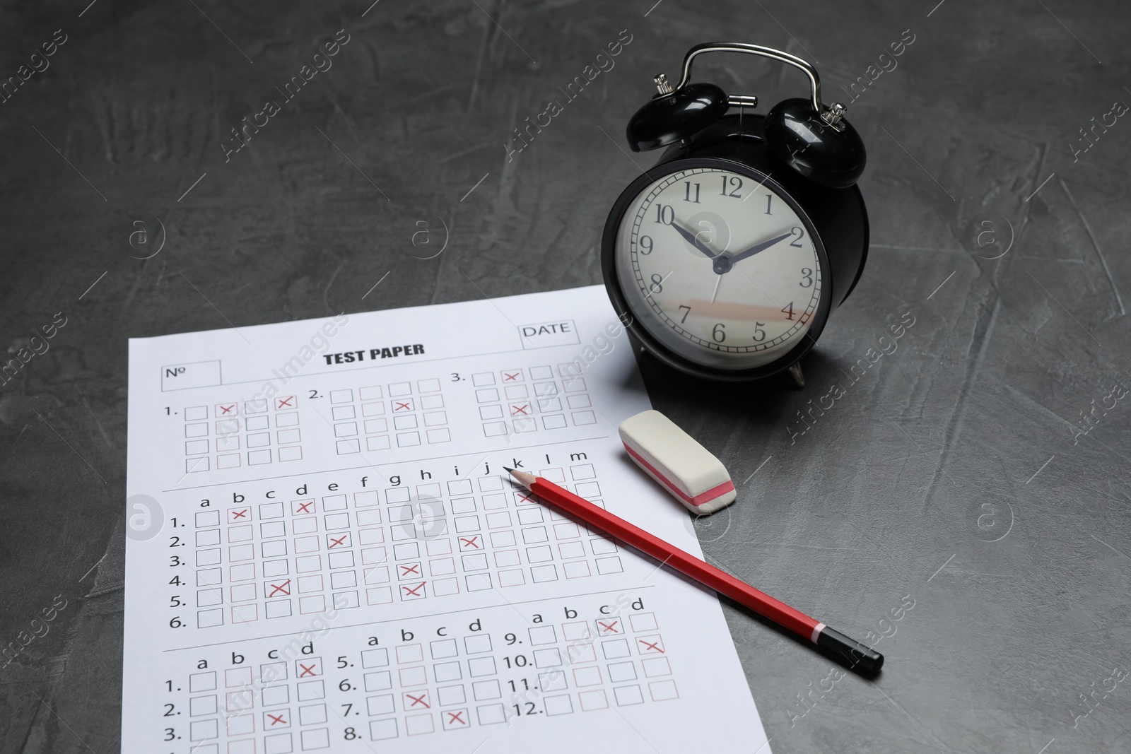 Photo of Answer sheet, alarm clock, pencil and eraser on gray textured table, closeup. Student passing exam