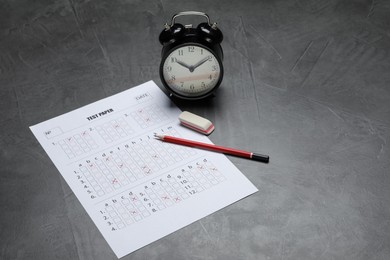 Photo of Answer sheet, alarm clock, pencil and eraser on gray textured table. Student passing exam