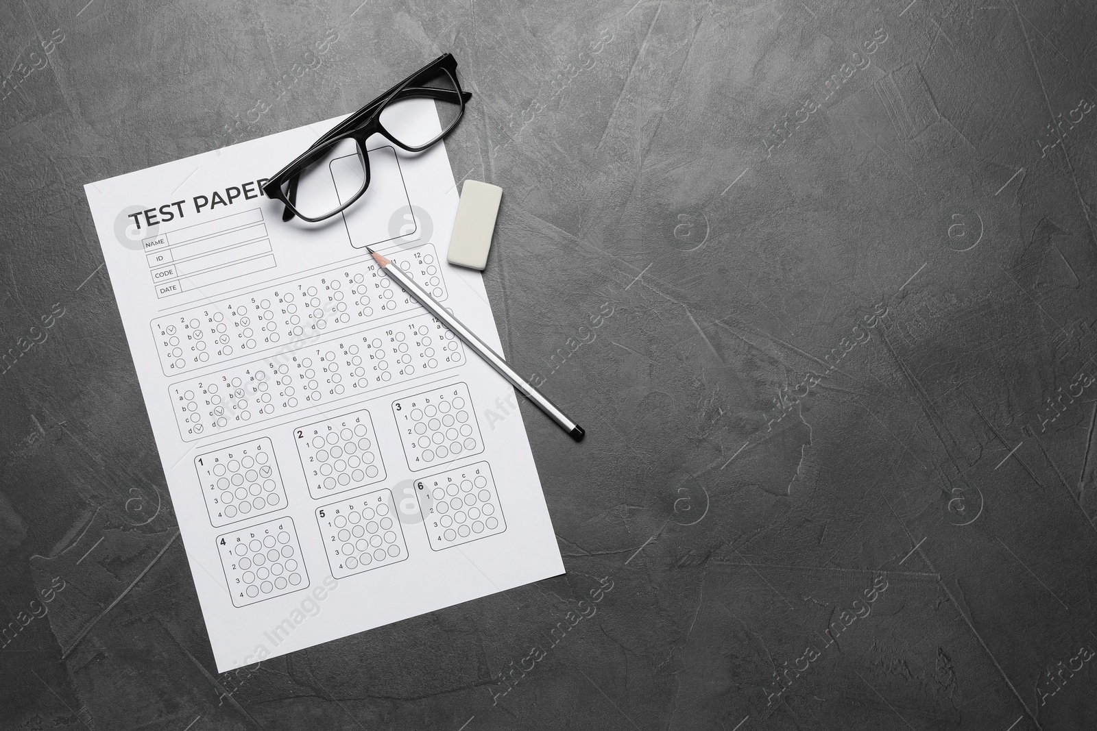 Student passing exam. Answer sheet, glasses, pencil and eraser on gray textured table, flat lay. Space for text Photo of Student passing exam. Answer sheet, glasses, pencil and eraser on gray textured table, flat lay. Space for text