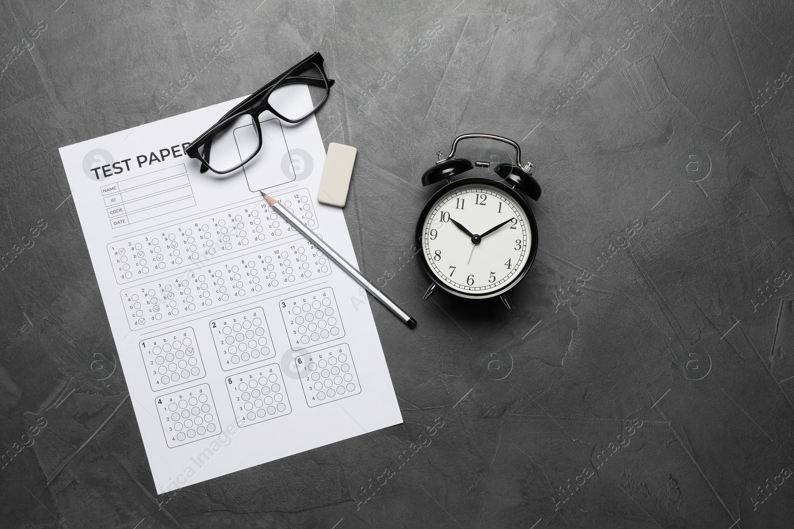 Answer sheet, alarm clock, glasses, pencil and eraser on gray textured table, flat lay. Student passing exam Photo of Answer sheet, alarm clock, glasses, pencil and eraser on gray textured table, flat lay. Student passing exam