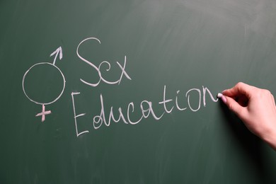 Photo of Woman writing word Sex Education on green chalkboard, closeup