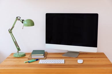 Photo of Home workspace. Modern computer, lamp and stationery on wooden desk indoors