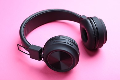 Photo of Pair of stylish black headphones on pink background, closeup