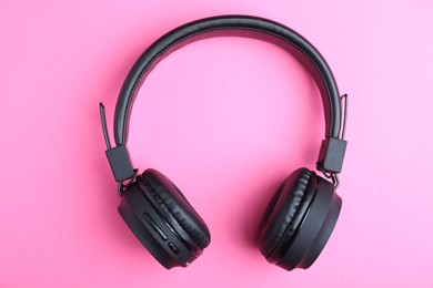Photo of Pair of stylish black headphones on pink background, top view