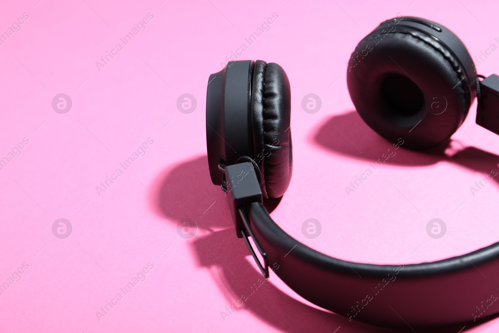 Pair of stylish black headphones on pink background, closeup. Space for text Photo of Pair of stylish black headphones on pink background, closeup. Space for text