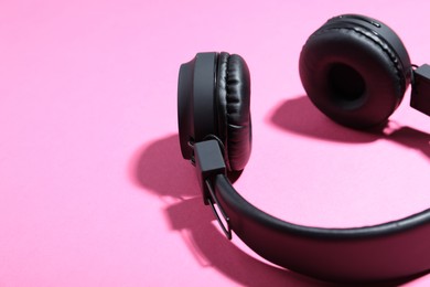 Photo of Pair of stylish black headphones on pink background, closeup. Space for text