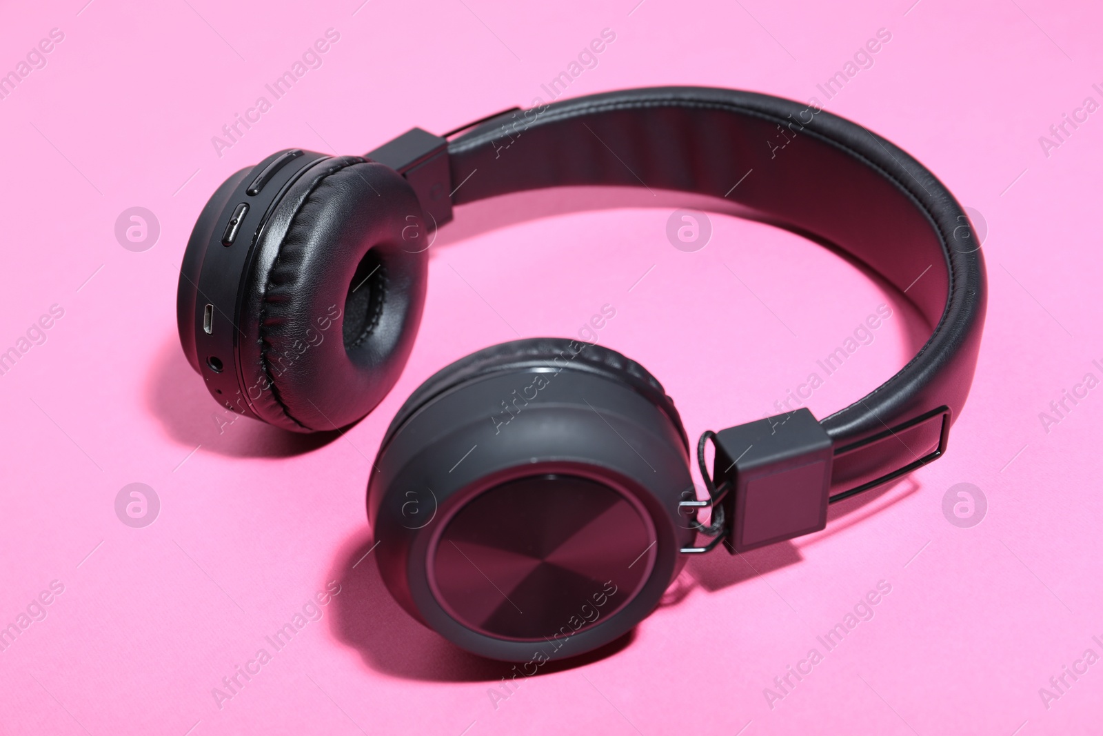 Pair of stylish black headphones on pink background, closeup Photo of Pair of stylish black headphones on pink background, closeup