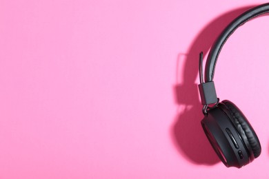 Photo of Pair of stylish black headphones on pink background, top view. Space for text