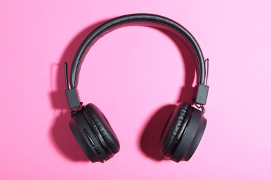 Photo of Pair of stylish black headphones on pink background, top view