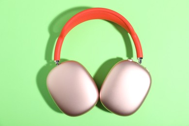Photo of Pair of stylish pink headphones on light green background, top view