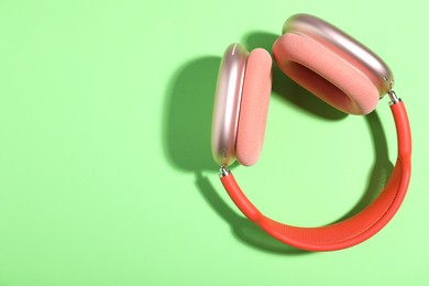 Photo of Pair of stylish pink headphones on light green background, top view. Space for text