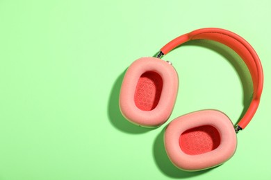 Photo of Pair of stylish pink headphones on light green background, top view. Space for text