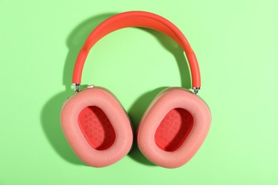 Photo of Pair of stylish pink headphones on light green background, top view