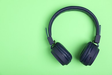 Photo of Pair of stylish blue headphones on light green background, top view. Space for text