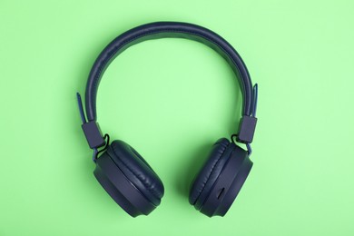 Photo of Pair of stylish blue headphones on light green background, top view