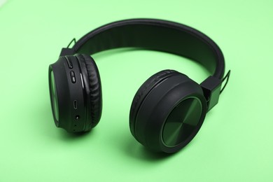 Photo of Pair of stylish black headphones on light green background, closeup