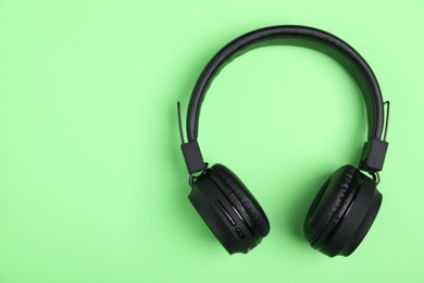 Photo of Pair of stylish black headphones on light green background, top view. Space for text
