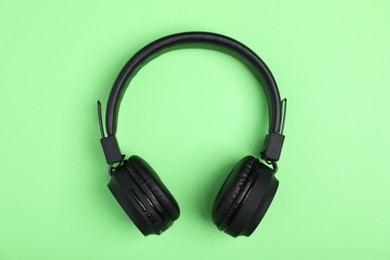 Photo of Pair of stylish black headphones on light green background, top view