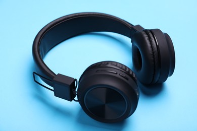 Photo of Pair of stylish black headphones on light blue background, closeup