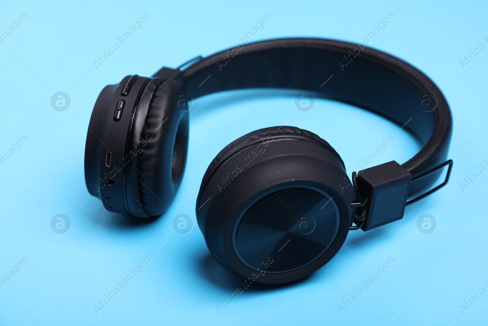 Pair of stylish black headphones on light blue background, closeup Photo of Pair of stylish black headphones on light blue background, closeup