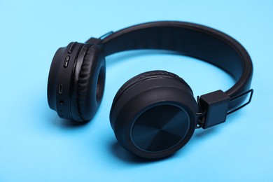 Photo of Pair of stylish black headphones on light blue background, closeup