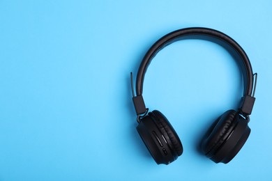Photo of Pair of stylish black headphones on light blue background, top view. Space for text